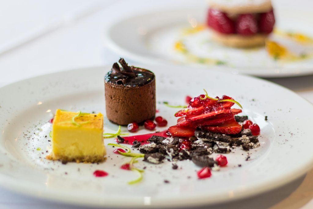 A visually appetizing assortment of gourmet desserts delicately arranged on a white plate, featuring chocolate mousse, cheesecake, and strawberry compote.