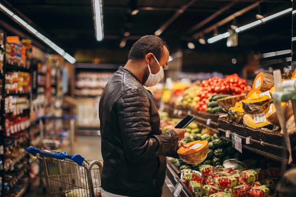 Man shopping in grocery store, inspecting fresh produce while wearing a mask.